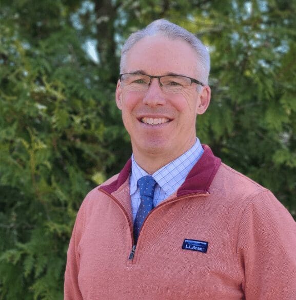 Dr. Jeffry Marlett smiles at the camera in front of a forest background.
