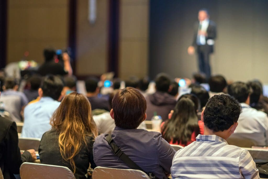 A man in a suit speaks to an audience of college students.
