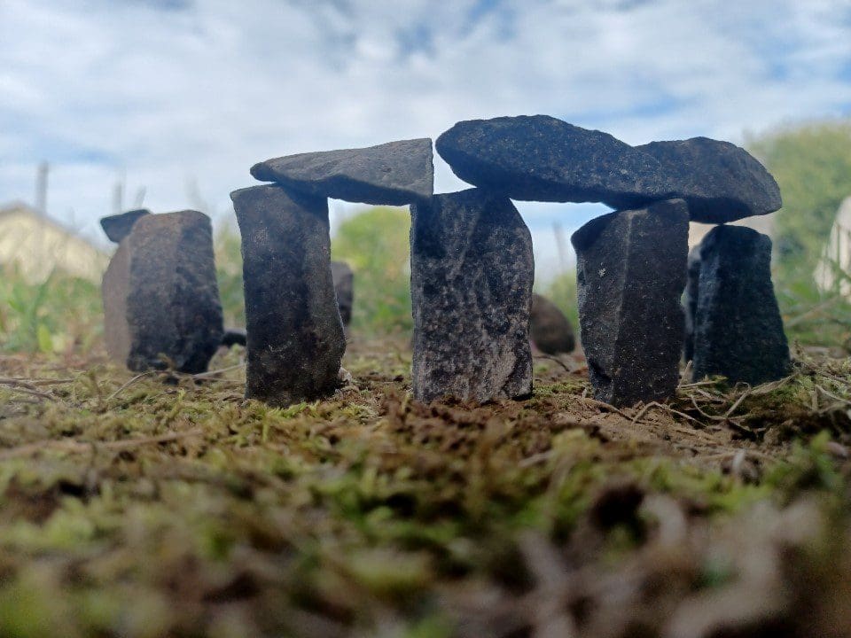 A tiny recreation of Stonehenge sits in the moss.