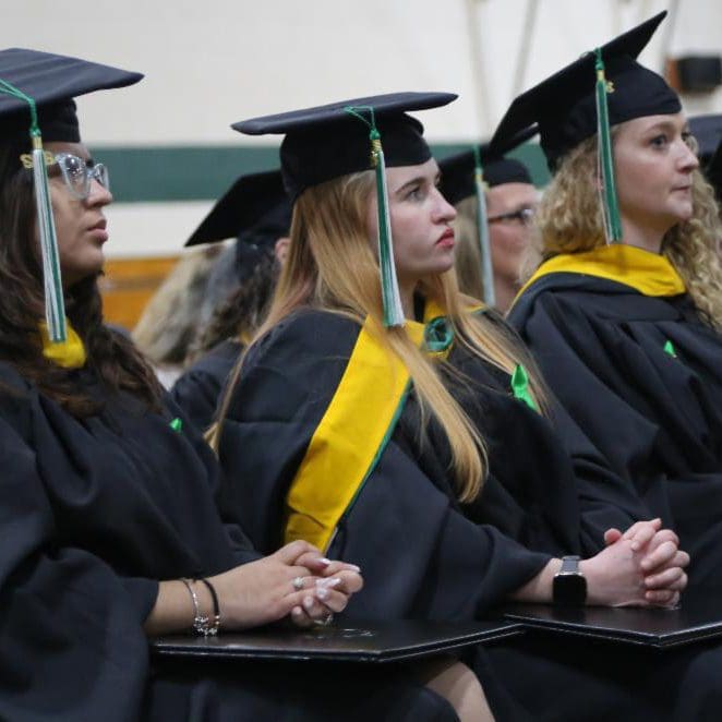 Three master's students sit and listen to a speaker at winter commencement.