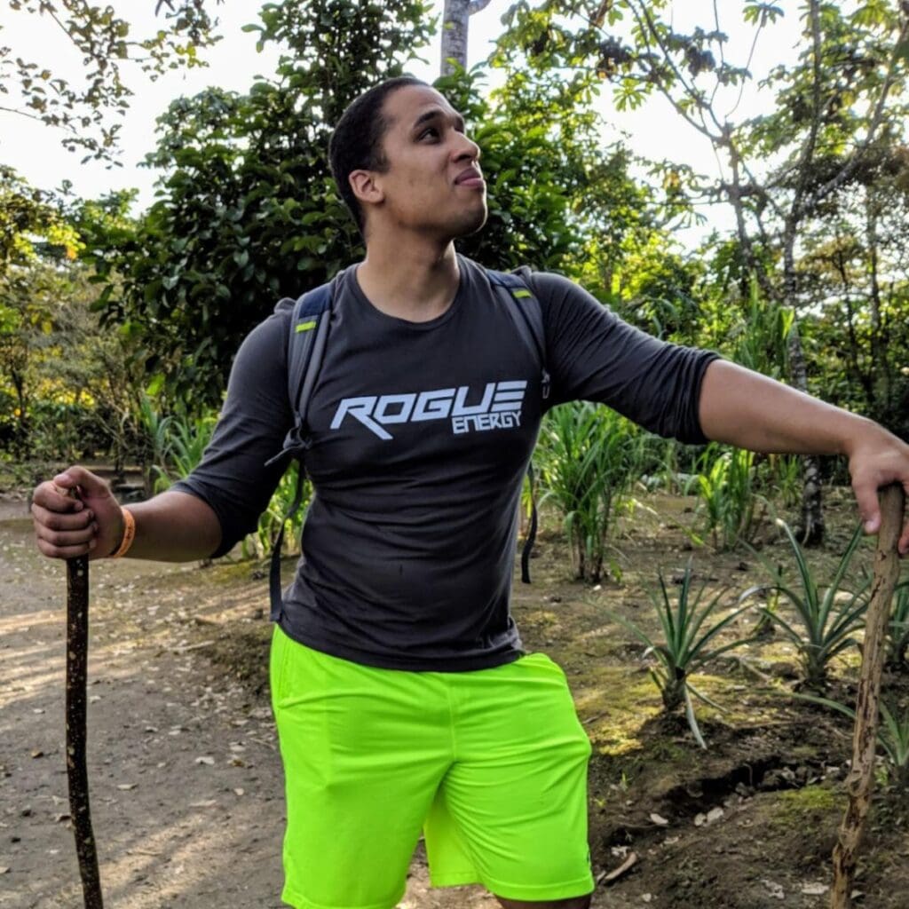 A young person in highlighter yellow shorts poses in front of the camera with a walking stick.
