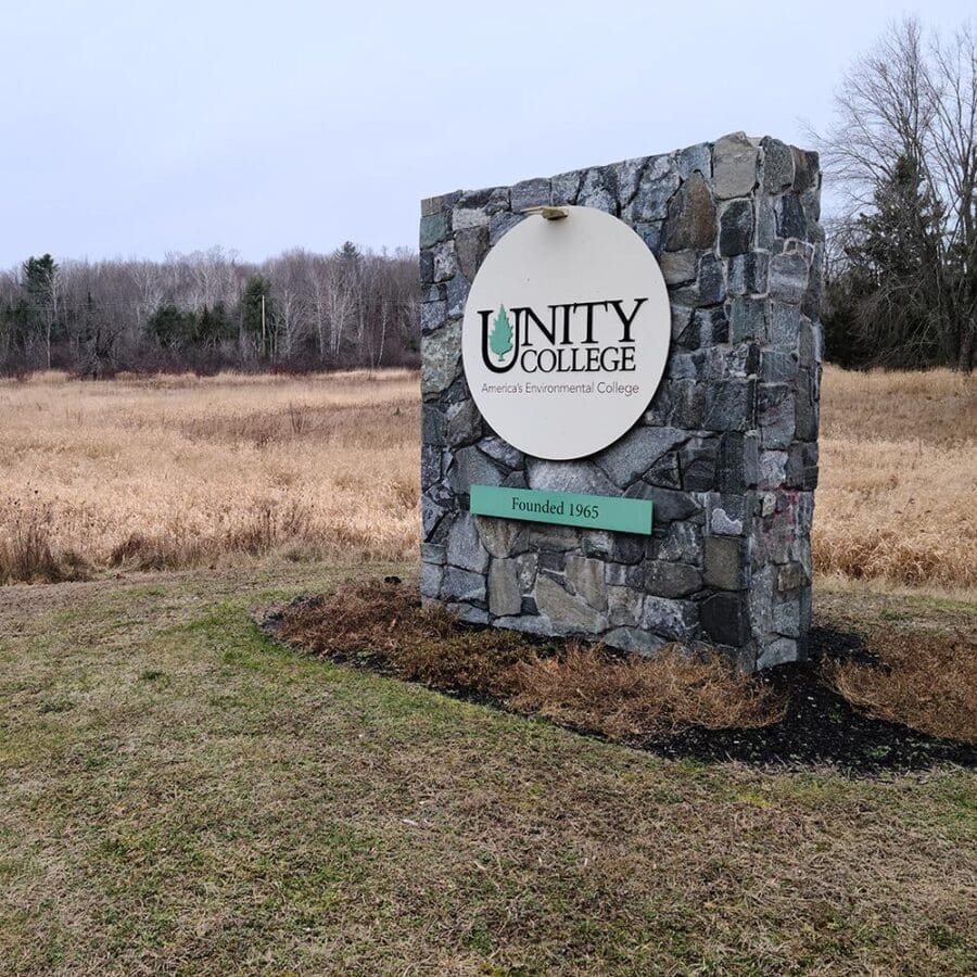 A large stone sign that says Unity Environmental University sits in a grassy field.