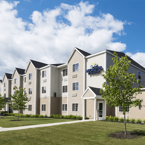 A row of khaki colored buildings sit in a grassy lawn in the sunshine.
