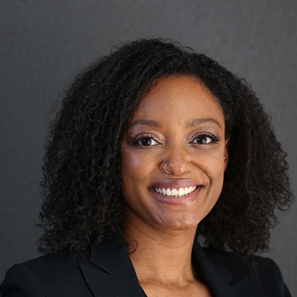 A woman smiles at the camera in front of a dark grey background.