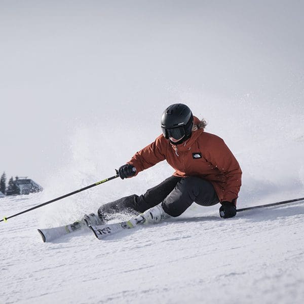 A person in a red jacket and black helmet and goggles races down a snowy slope.