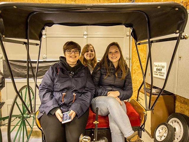 Three students smile at the camera from the cab of a classic automobile during an expedition course.