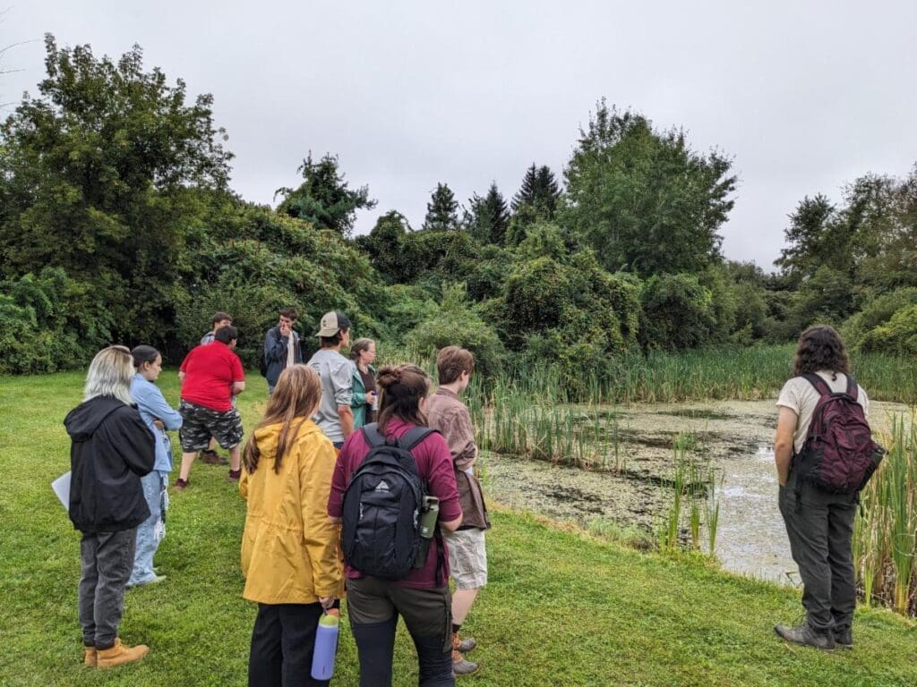 A colorful group of students gather at the edge of a pond.