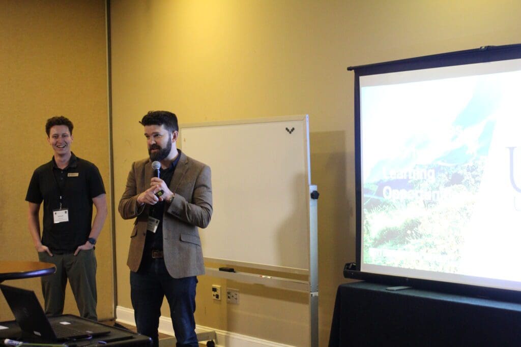 Two faculty members stand in front of a screen in a yellow room to give their presentation about AI.