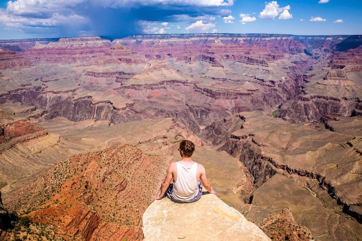a person sitting on the edge of a cliff looking out at endless possibilities