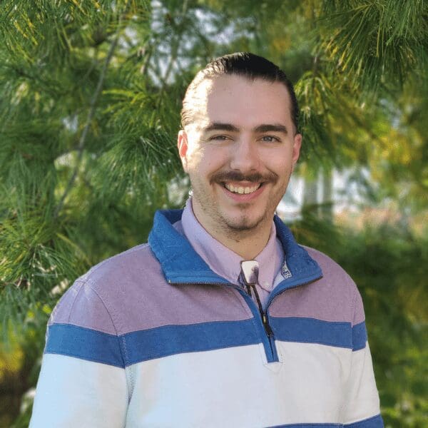 Sage Whitecloud smiles at the camera in a blue, white, and pink pullover.