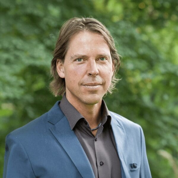 Dr. Sebastian Kretschmer smiles at the camera in front of a forest background.