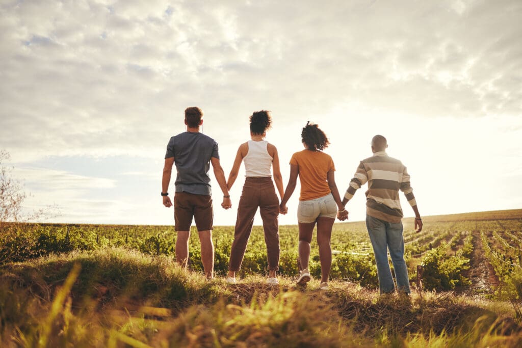 Four people hold hands together in a grassy field.