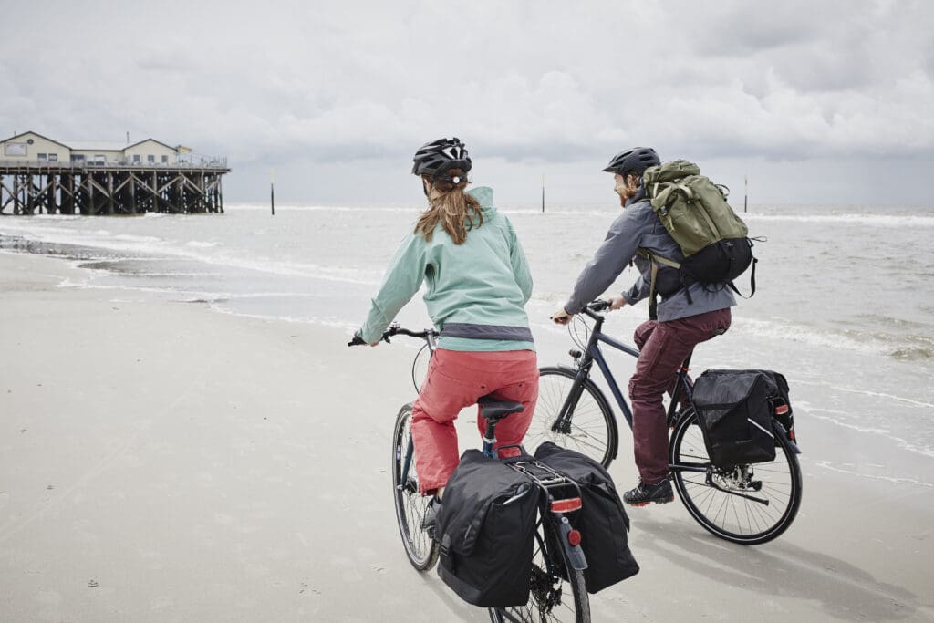 Germany, Schleswig-Holstein, St Peter-Ording, couple riding bicycle on the beach.