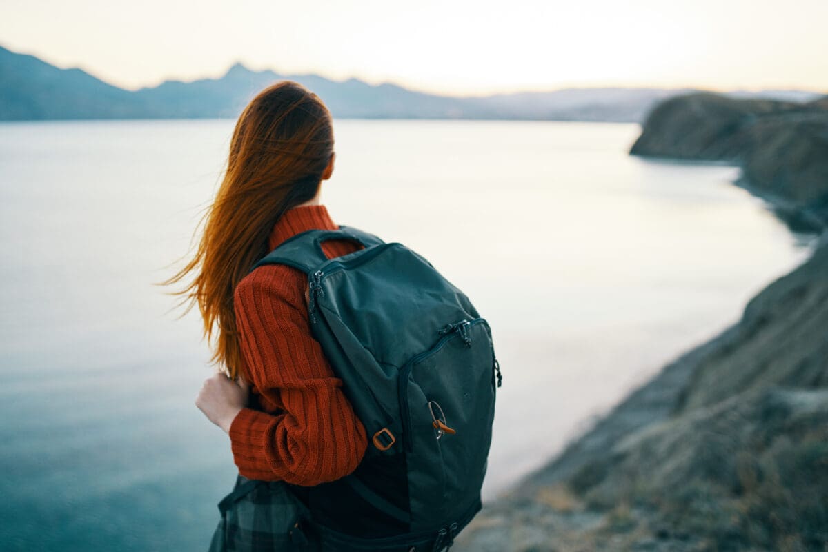 A woman in red sweater with backpack and travel tourism sea mountains back view. 