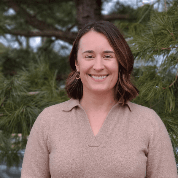 Allie smiles in front of a forest background in a tan shirt.
