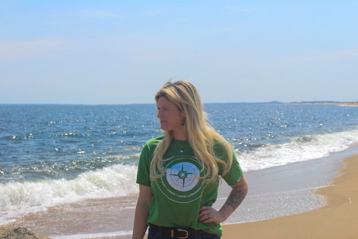 Kristin D is a student of Unity Environmental University standing on a beach in a green shirt.