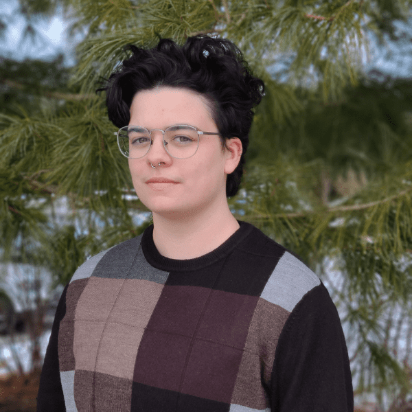Advisor, Alex Beaze, gazes at the camera in front of a forest background.