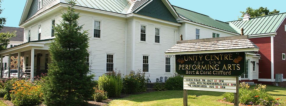 A white building with the sign for the Unity Performing Arts Center in front of it.