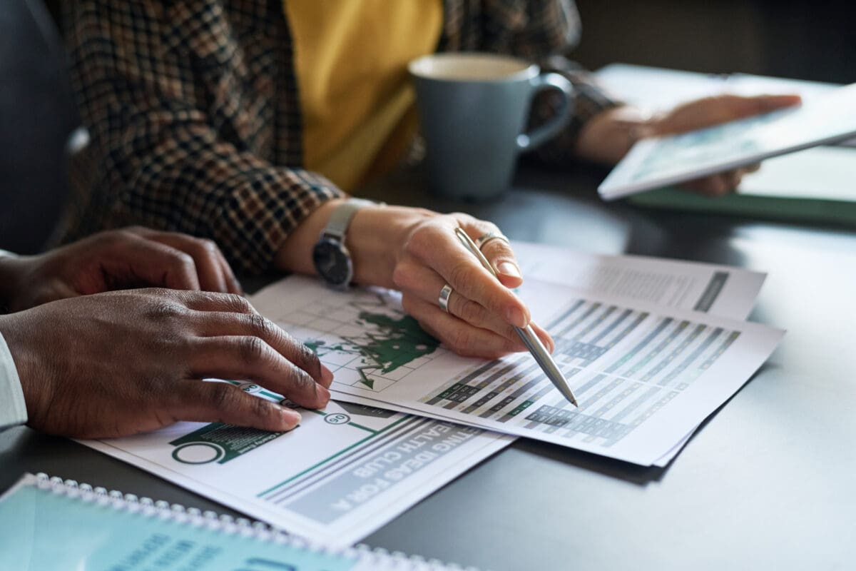 Close-up of businesswoman pointing at report with graphs and discussing it with her partner at meeting