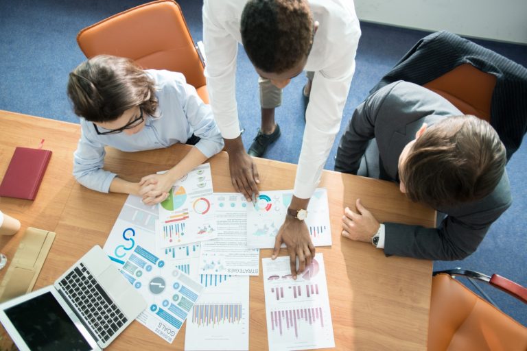 Directly above view of concentrated multi-ethnic marketing team in formalwear working together: they analyzing statistics and comparing data at meeting