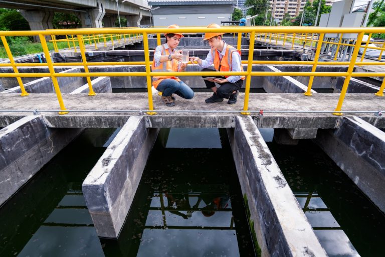 Two engineers take samples at a wastewater pond.