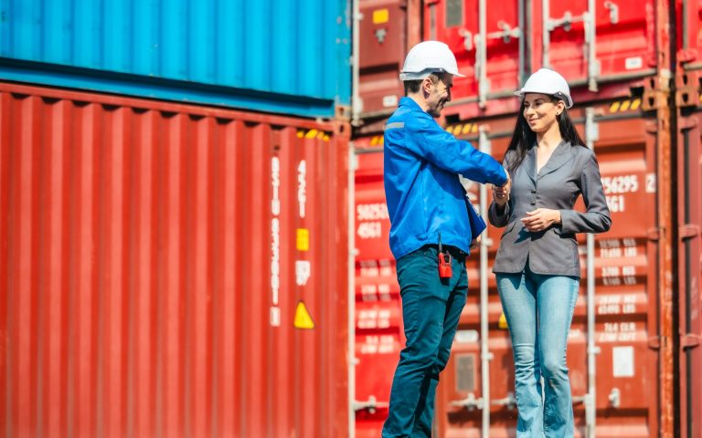 Industrial container workers discussing eco-friendly logistics strategies. Reducing fuel consumption, lowering carbon footprints, and implementing zero-emission practices in supply chain operations.