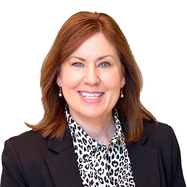 A woman with red hair in a spotted shirt and black blazer smiles at the camera.