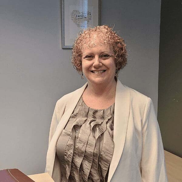 A woman in a grey dress and white sweater smiles at the camera.