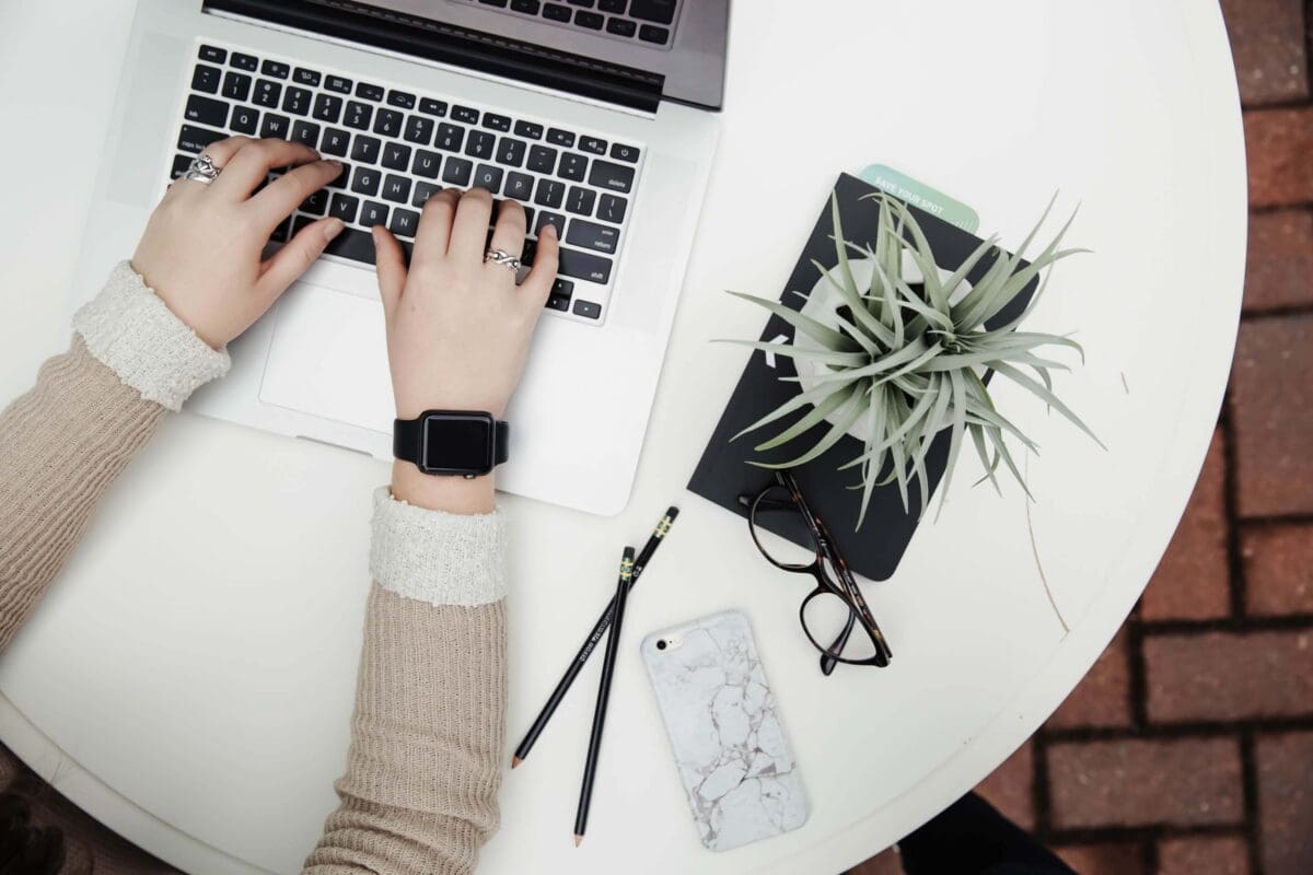 a person typing on a computer with a plant on the table