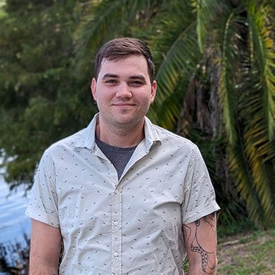 A young man, Nevan Burns, in a white a speckled button up smiles at the camera.