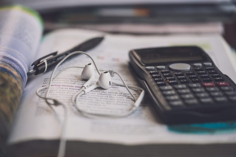 Closeup shot of headphones, calculator, and pen on book