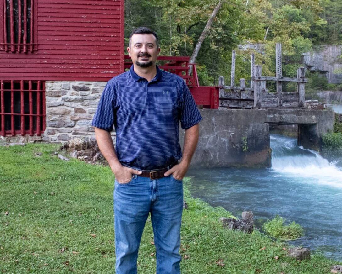 Unity student Ron standing by a waterfall and red barn.