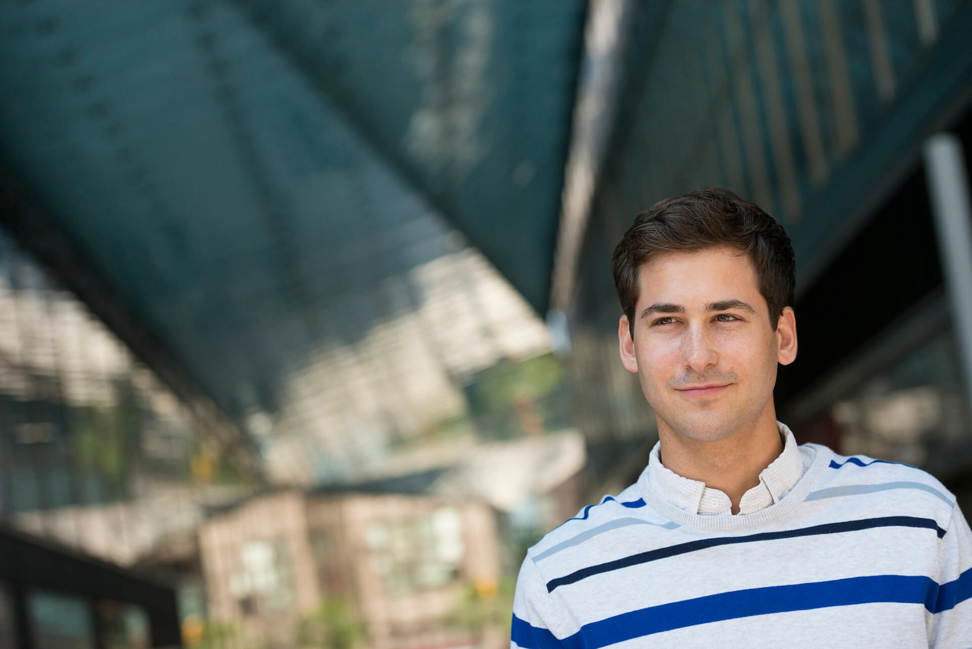 Business Casual,USA,Outdoors in the city. In a public space. Business people on the move. A young man in a striped sweater looking into the distance.