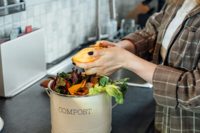 Compost the kitchen waste, recycling at home. Woman putting vegetables cutted leftovers into the garbage, compost bin on the table of kitchen. Environmentally responsible, ecology. Selective focus