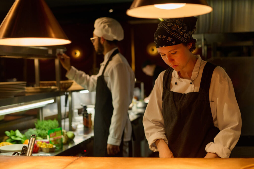 Young serious female worker of restaurant preparing food in the kitchen